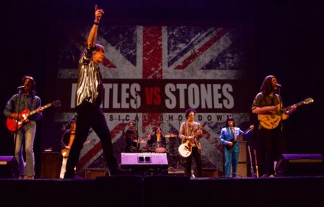 Beatles vs. Stones tribute band performs on stage with a British flag and "Musical Showdown" backdrop.