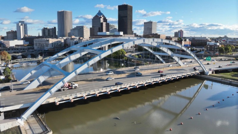 Aerial view of the Douglass-Anthony bridge over a river with cars, leading to the Rochester, NY skyline.