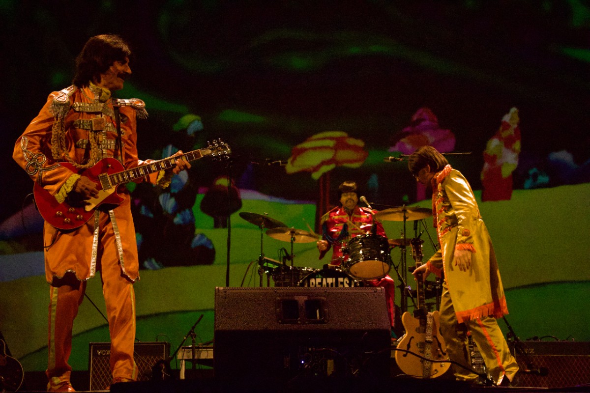 A Beatles tribute band performs on stage with "Yellow Submarine" backdrop imagery at a Finger Lakes venue.