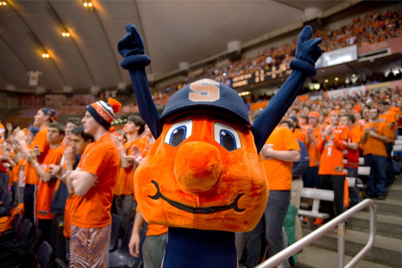 Syracuse University mascot Otto the Orange with arms raised in the Carrier Dome, surrounded by fans in orange.