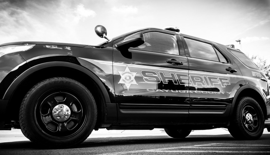 A black and white photo of a Cayuga County Sheriff's Office patrol SUV parked outdoors.