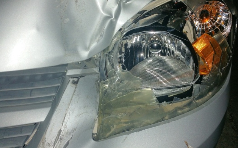 Close-up of a silver car's front with a shattered headlight and crumpled fender after an accident.