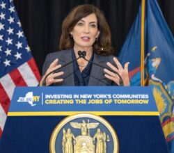 New York Governor Kathy Hochul speaks at a podium with state branding and flags behind her.
