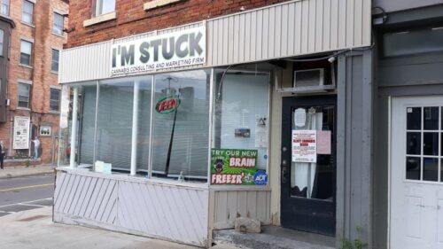 Storefront of 'I'M STUCK Cannabis Consulting and Marketing Firm' with a 'STOP LAWLESSNESS' sign on the door.