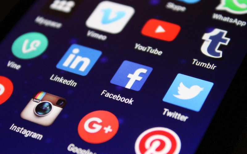 A close-up of a smartphone screen displaying various social media app icons like Facebook, Twitter, Instagram, and LinkedIn.