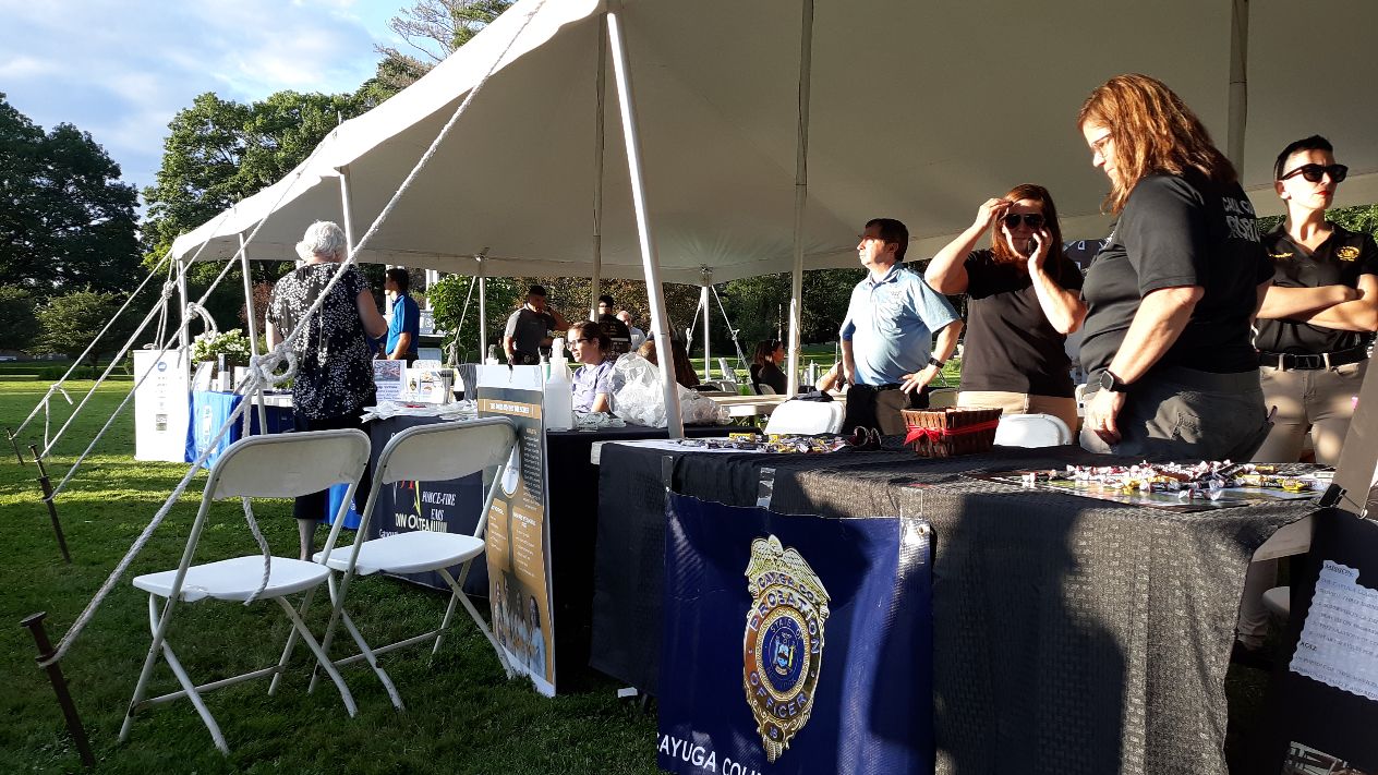 People staff a booth for Ayuga County Probation Department under a tent at an outdoor community event.