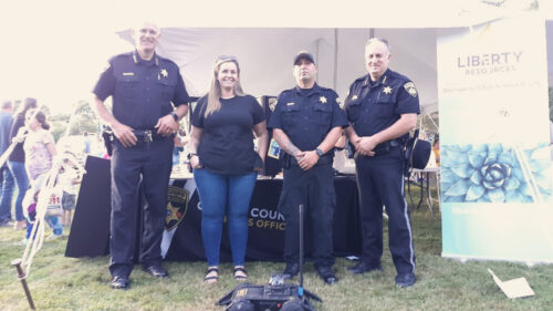 Three sheriffs and a woman stand with a robot at a County Sheriff's Office community event booth.