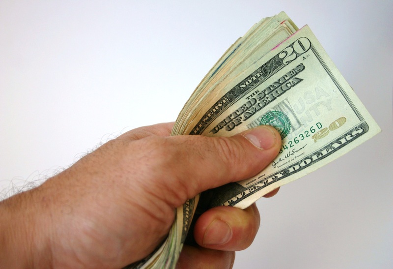 A hand holds a stack of US twenty-dollar bills against a plain white background.