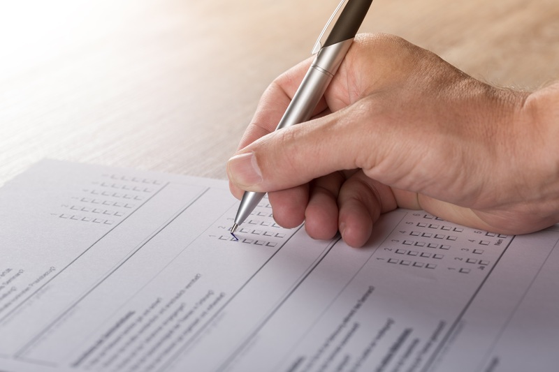 A hand holds a pen, marking a checkbox on a paper form or survey.