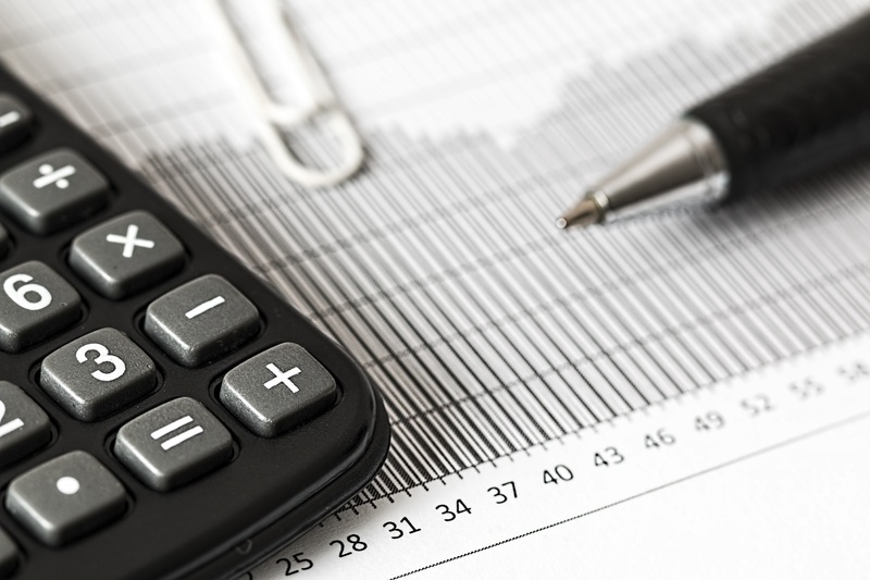 A calculator, pen, and financial document with numbers and graphs on a desk.