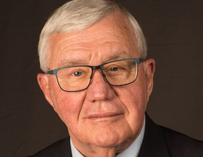 Headshot of Carl Blowers, an older man with white hair and glasses, wearing a dark suit.