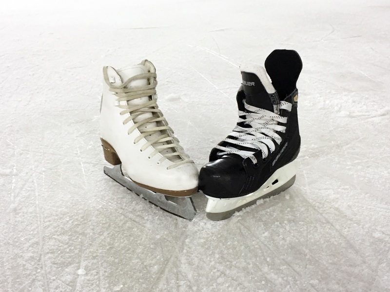 A white figure skate and a black hockey skate stand side-by-side on an ice rink.