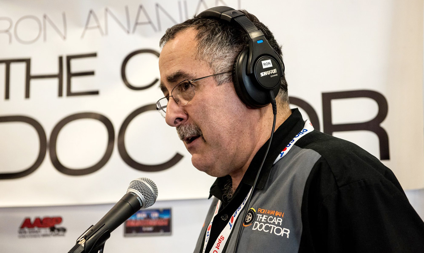 Ron Ananian, "The Car Doctor," speaks into a microphone while wearing headphones at an event.