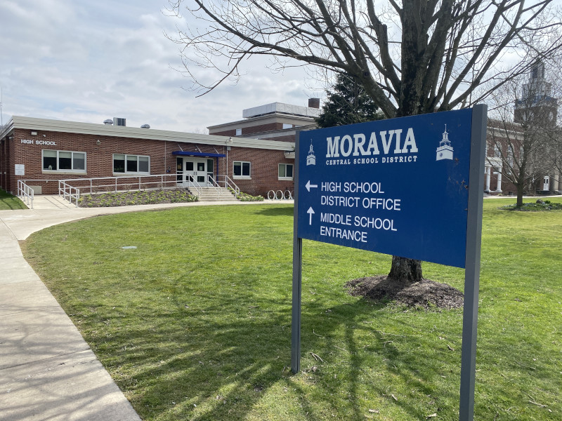 A blue sign for Moravia Central School District with directions to the high school, district office, and middle school entrance.