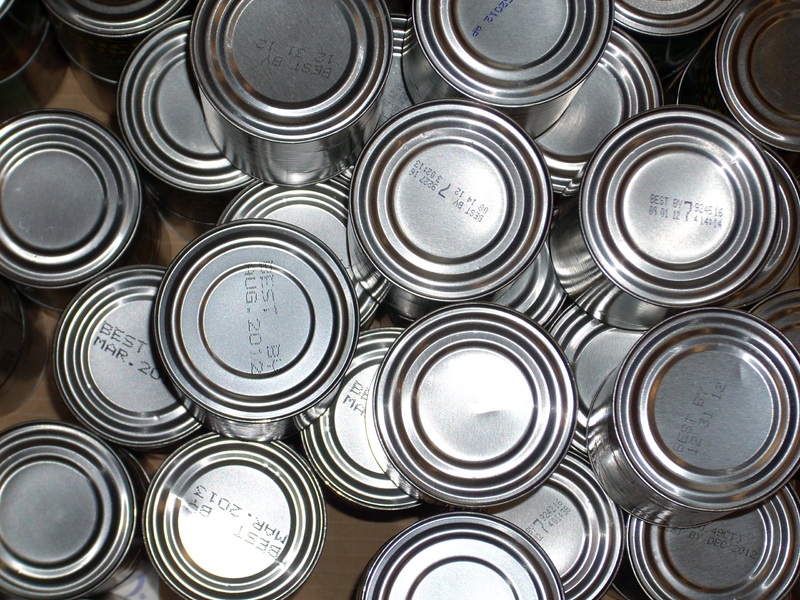 Overhead shot of many silver canned goods with visible 'Best By' dates on their tops.