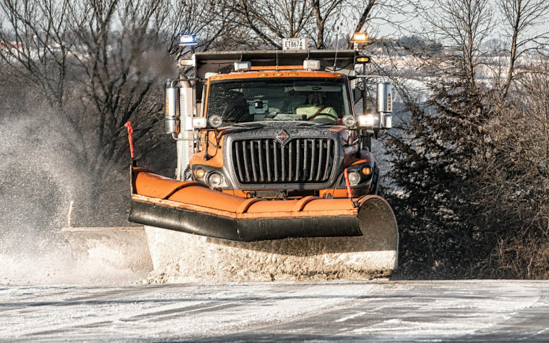 An orange snowplow sprays snow as it clears a road in the Finger Lakes region.