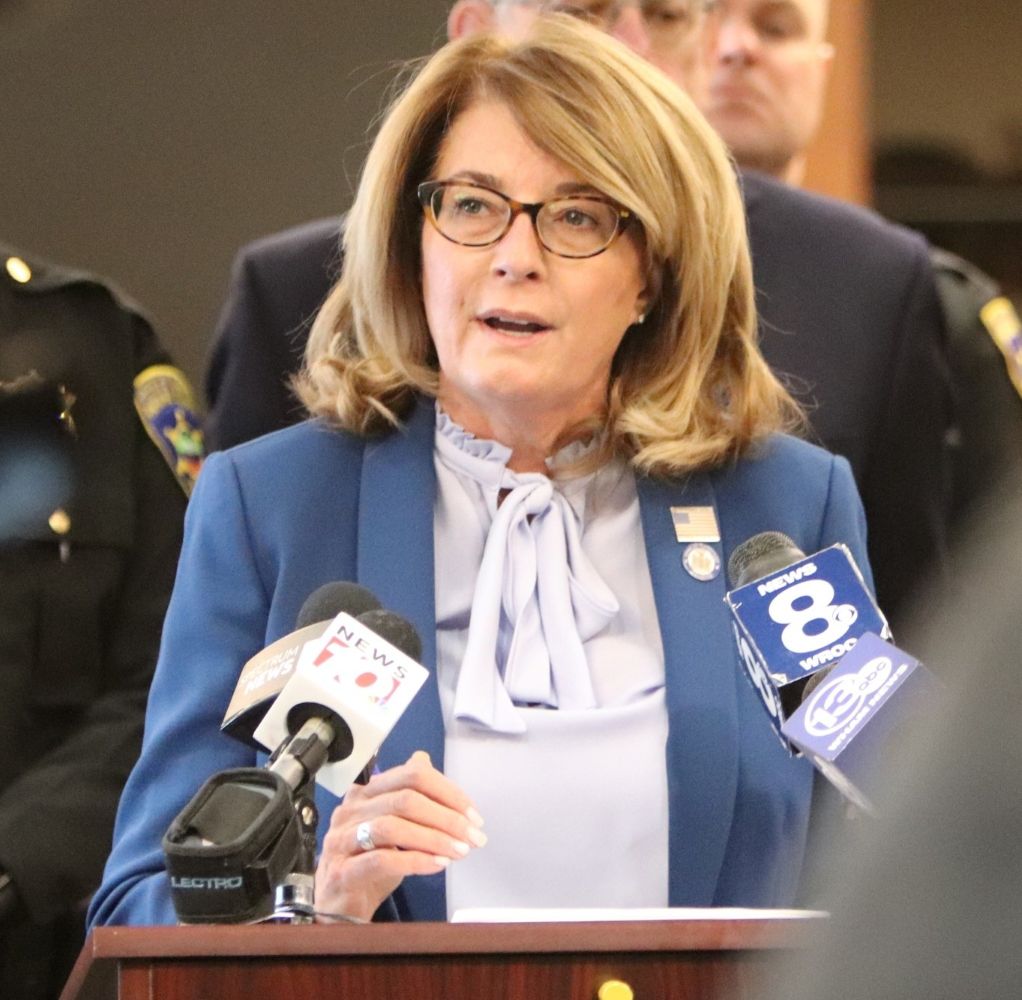 State Senator Pam Helming speaks at a podium with microphones, including NEWS 8 and WROC, at a press event.