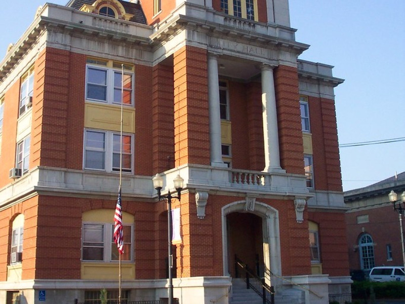 Exterior of Geneva City Hall, a brick and stone building with prominent columns and a U.S. flag.