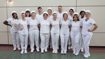 Group of 17 graduating nursing students in white uniforms posing for a photo.