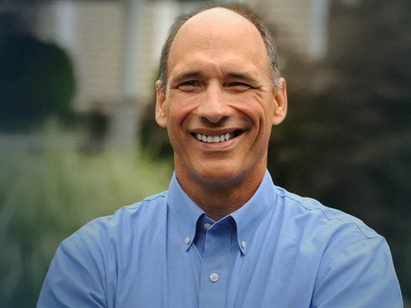 Smiling portrait of Assemblyman John Lemondes in a blue button-down shirt outdoors.