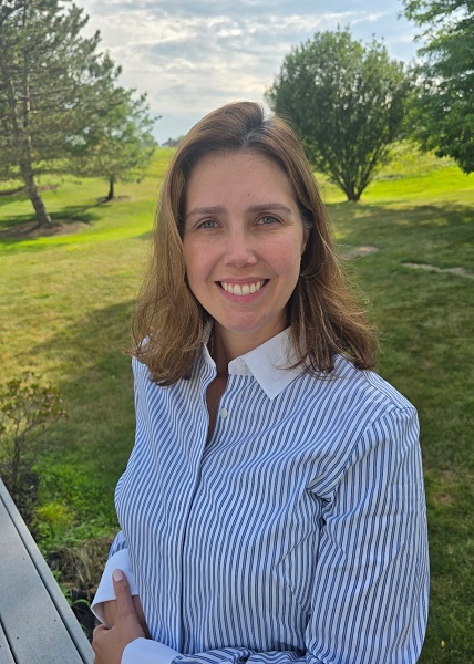 Smiling woman Mariana Aurich in a striped shirt stands outdoors with a green lawn and trees in the background.