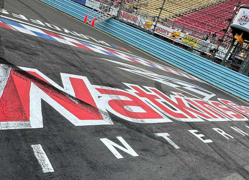 The Nationwide logo and 'PLAYOFFS' are painted on the asphalt track at Watkins Glen International, with empty grandstands in the background.