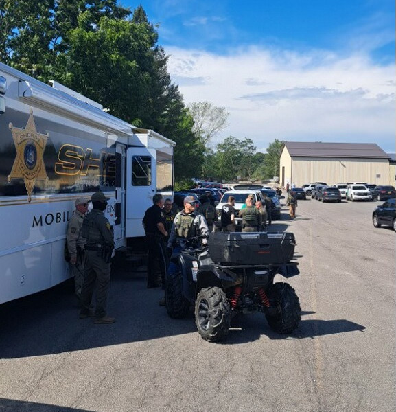 Sheriff's deputies stand near a Mobile Command Center and ATV in a parking lot.