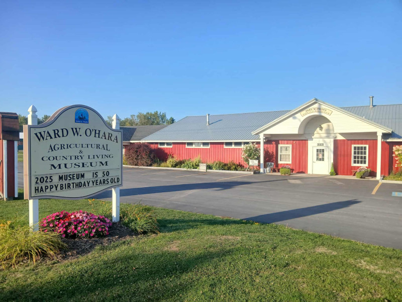 Exterior of the Ward W. O'Hara Agricultural & Country Living Museum, a red building with a sign, under a clear blue sky.