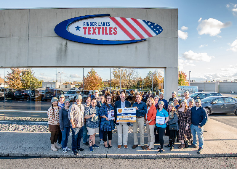 Group poses outside Finger Lakes Textiles building with a "FLX Chamber" welcome sign for a business event.
