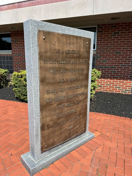 Granite memorial plaque honoring Yates County soldiers and sailors, set on a brick path outside a building.