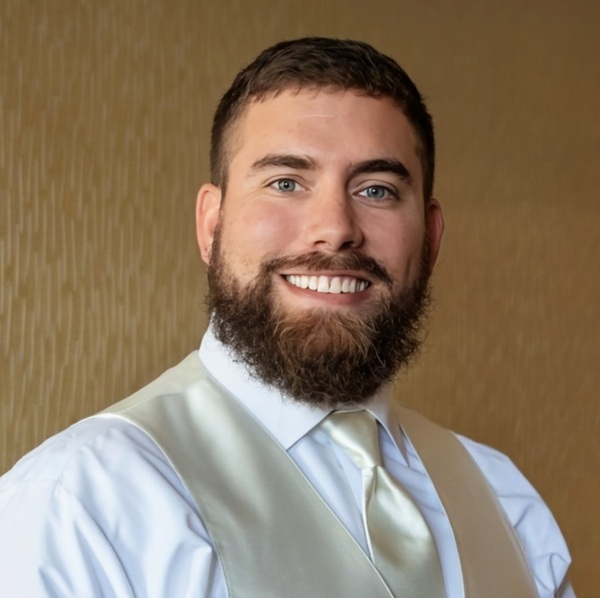 Smiling man with a beard wearing a white shirt, light vest, and tie.