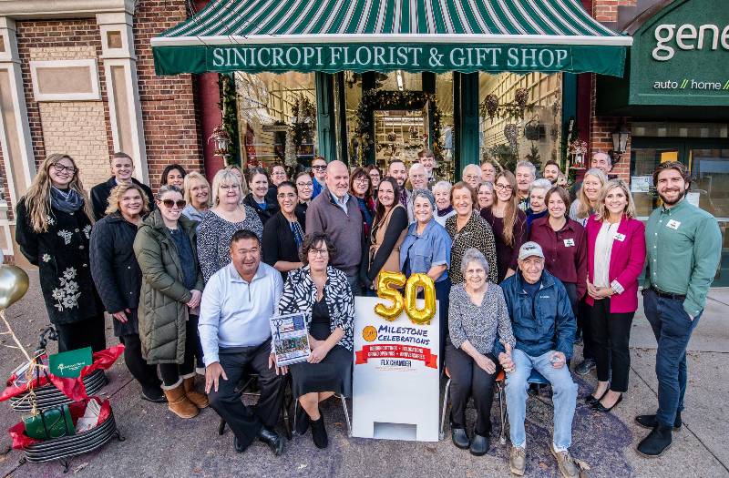 Large group poses outside Sinicropi Florist & Gift Shop with a "50 Milestone Celebrations" sign.