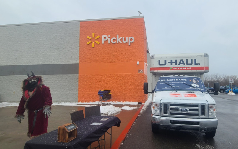 Krampus stands by a donation table outside Walmart Pickup, next to an A.P.E. Scare & Care U-Haul truck.