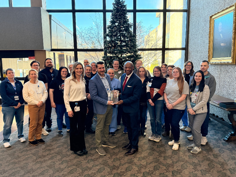 Hospital officials and staff pose with an award in a lobby with a Christmas tree.