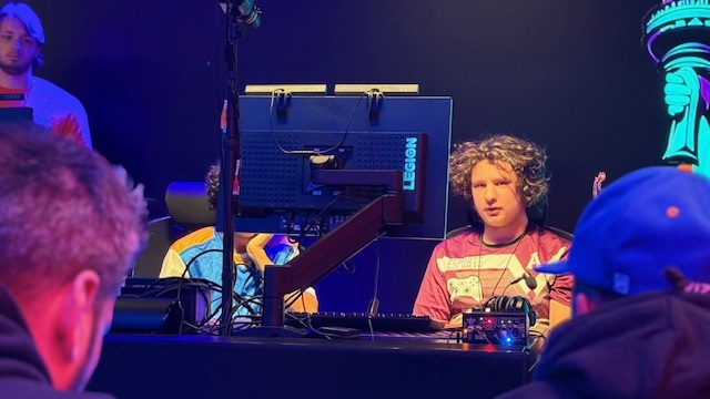 Young male esports athlete in a patterned jersey competes at a gaming PC, with a Legion monitor visible.