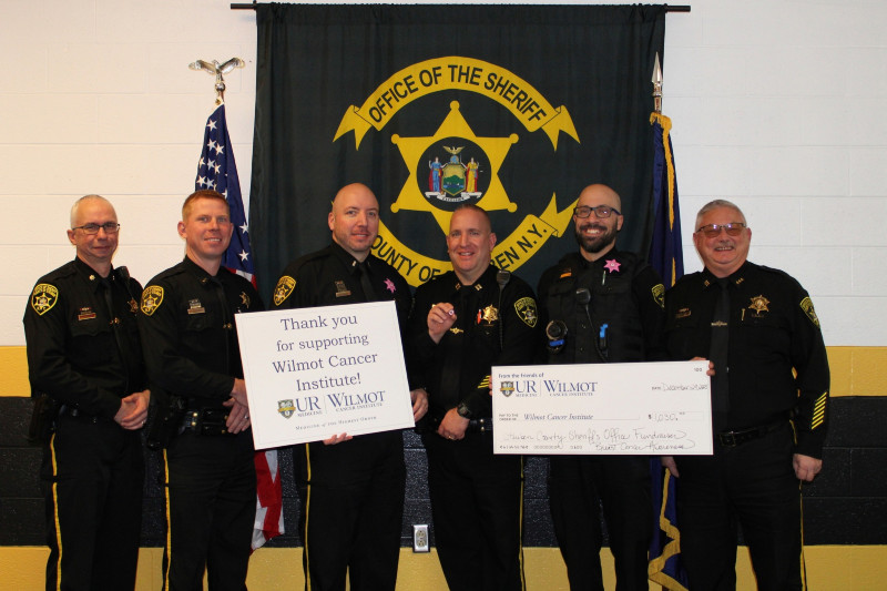 Six Steuben County Sheriff's officers present a $1,000 check to Wilmot Cancer Institute, holding a thank you sign.