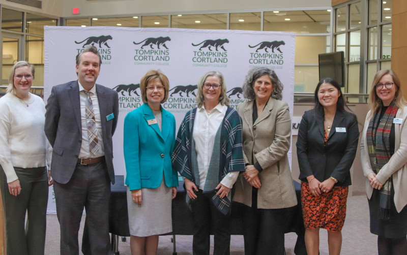 Seven people, including college officials, pose in front of a Tompkins Cortland Community College banner.