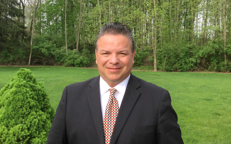 Michael Printup, former Watkins Glen International President, smiles outdoors in a suit and tie.