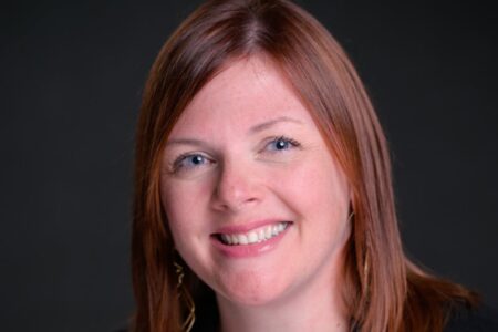 Headshot of Amie Hendrix, outgoing City Manager of Geneva, smiling against a dark background.