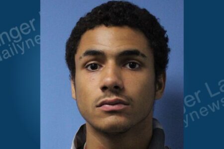 Mugshot of Ashton Norson, a young man with dark curly hair and a light mustache, looking forward.