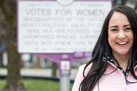 Auburn native Buller smiles in front of a 'Votes for Women' historical marker in Cayuga County.