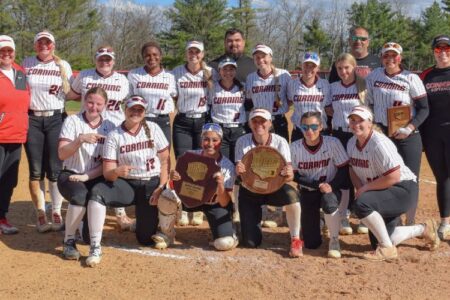 The SUNY Corning softball team celebrates their regional championship victory with trophies on the field.