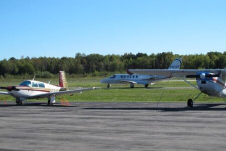 Three airplanes, including two propeller planes and a small jet, parked on the tarmac at Canandaigua Airport.