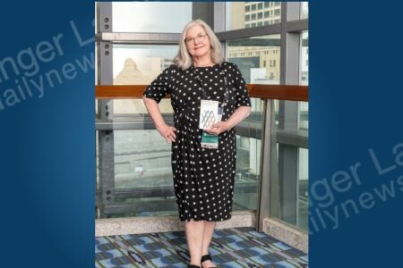 Woman in polka-dot dress holding an award, celebrating Seward House Museum's national recognition.