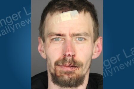 Mugshot of a man with a bandage on his forehead and visible injuries around his nose and mouth.