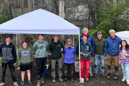 Volunteers, including adults and youth, stand under a tent after planting a tiny forest in Dryden.