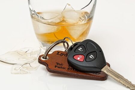 Car keys next to a broken glass of whiskey with ice, symbolizing the dangers of impaired driving.