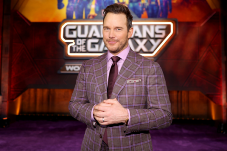 Chris Pratt smiles in a plaid suit before a "Guardians of the Galaxy" backdrop.