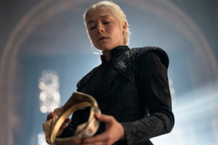 Emma D'Arcy as Rhaenyra Targaryen, with platinum blonde hair, holding a crown and looking down.