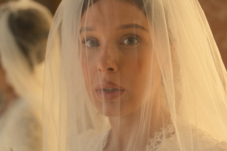 Millie Bobby Brown as Enola Holmes, a bride-to-be, looks surprised through her wedding veil, solving a new mystery.